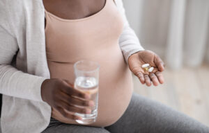 Pregnant woman taking pills capsules and glass of water